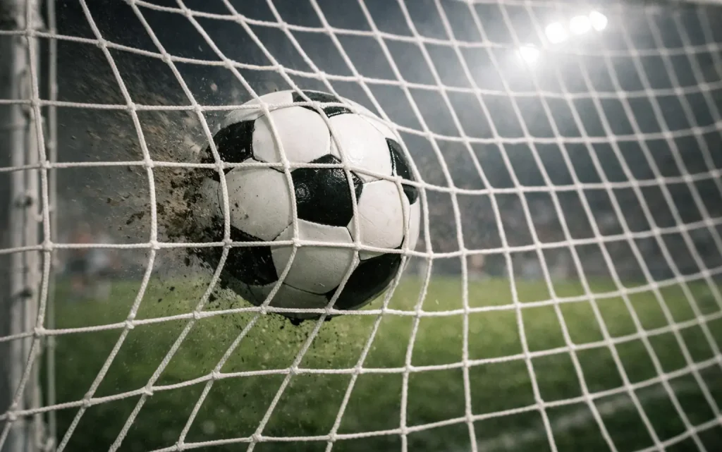 Pallone da calcio che entra nella rete di una porta durante una partita serale